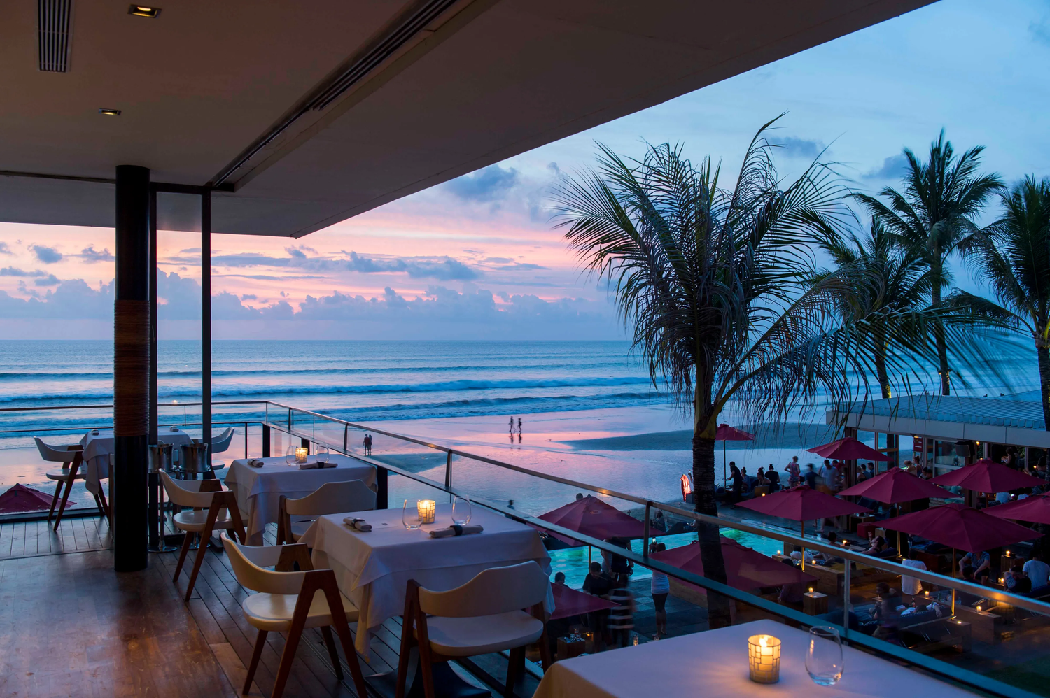 An open-air dining terrace and palms overlooking the ocean at sunset